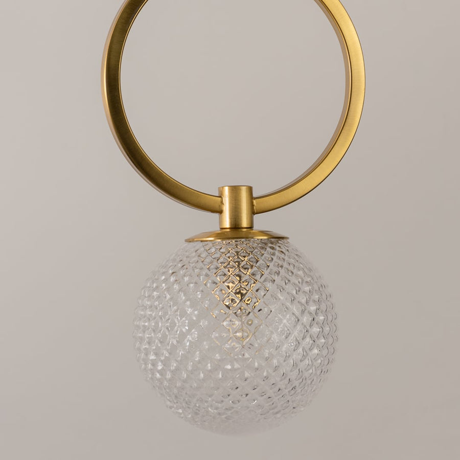 Closeup of gold ring pendant light showing detailed textured glass globe and smooth metallic finish with warm illumination.