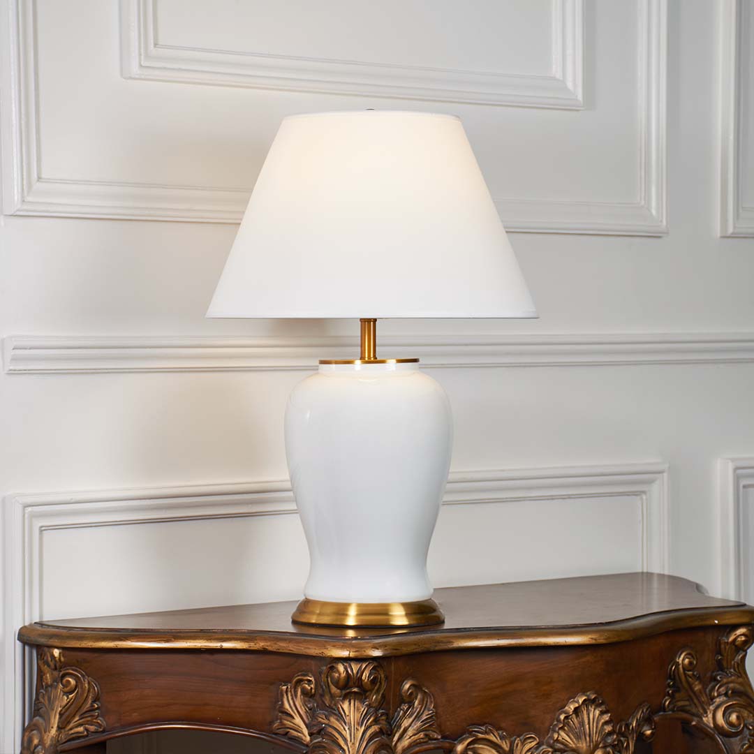 White ceramic table lamp with gold metal base and cone fabric shade illuminated on a white background for elegant home lighting presentation.