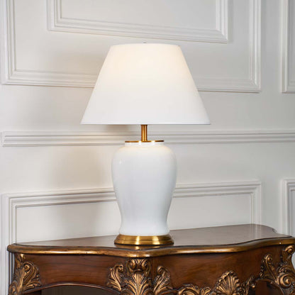 White ceramic table lamp with gold metal base and cone fabric shade illuminated on a white background for elegant home lighting presentation.