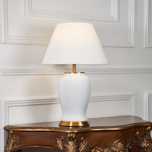 White ceramic table lamp with gold metal base and cone fabric shade illuminated on a white background for elegant home lighting presentation.