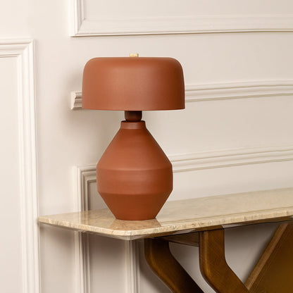 Terracotta table lamp with sculptural ceramic base and matching shade styled on shelf in modern living space.