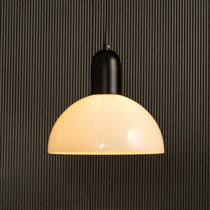 A warm glowing dome pendant light with a matte black top hanging before a ribbed dark backdrop adding soft illumination and stylish modern interior décor.