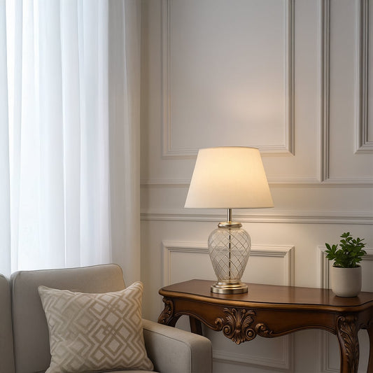 Elegant table lamp with glass base and white lampshade placed on a wooden console in a classic living room decor.