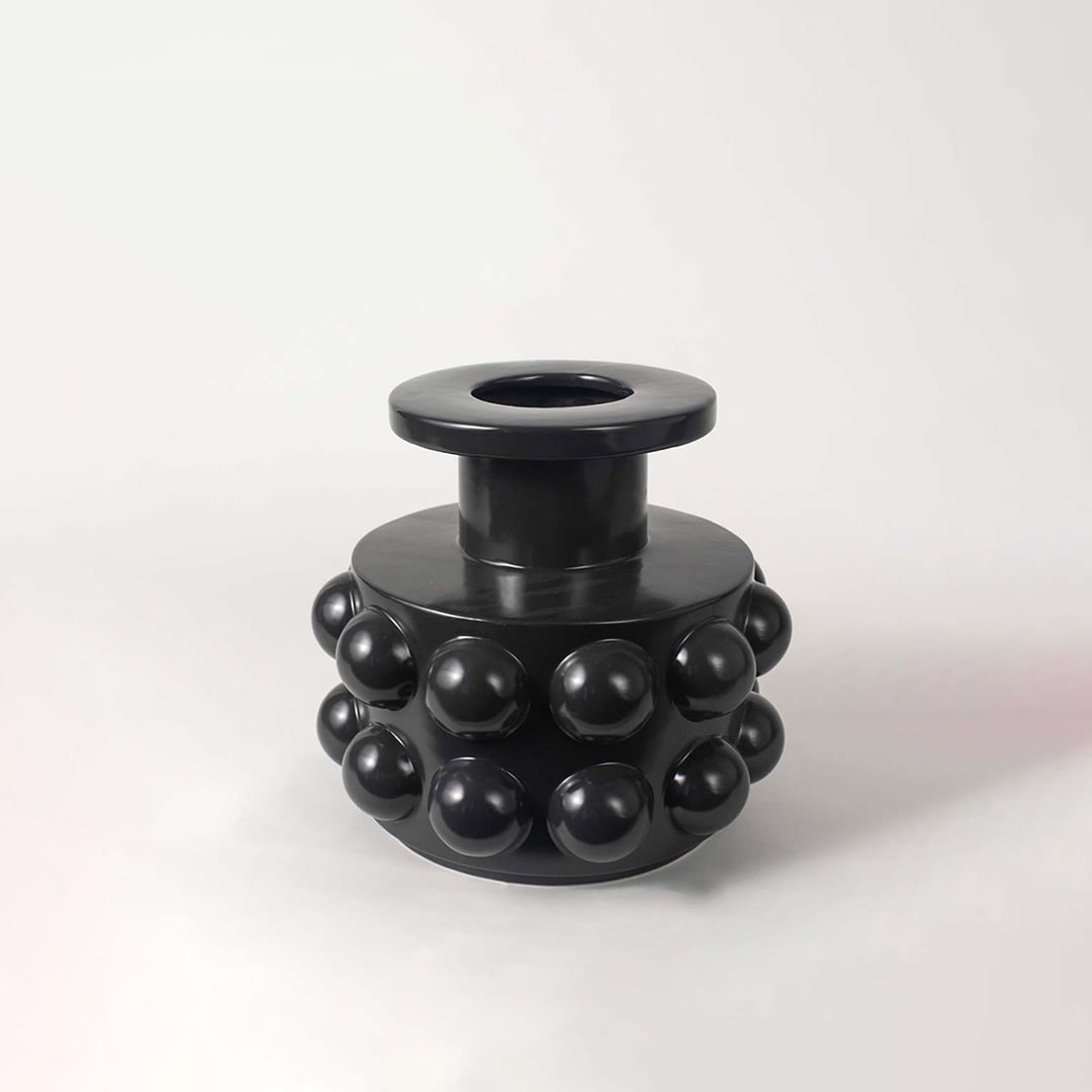 Modern black ceramic vase showcasing bubble-inspired round textures and sculptural cylindrical body on a white backdrop.