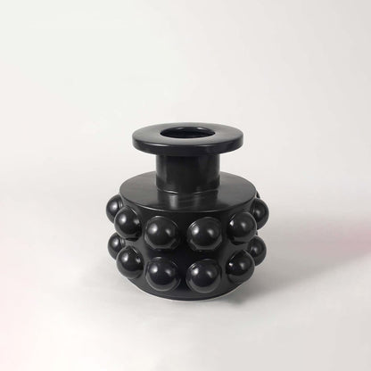 Modern black ceramic vase showcasing bubble-inspired round textures and sculptural cylindrical body on a white backdrop.