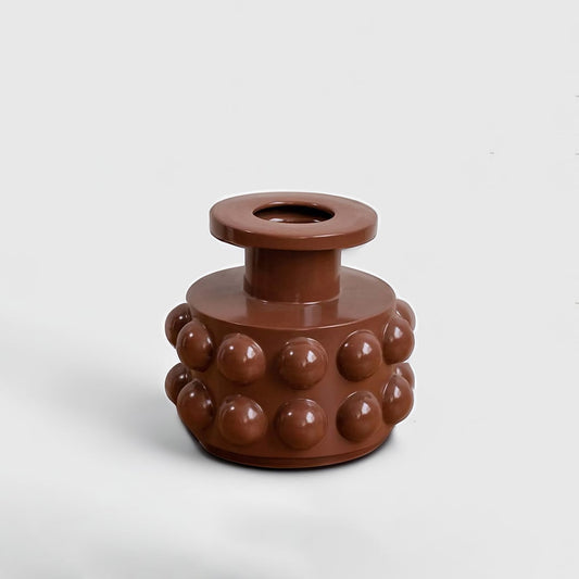 A modern brown sculptural vase with bold raised circular details displayed on a clean white background showing its artistic contemporary form.