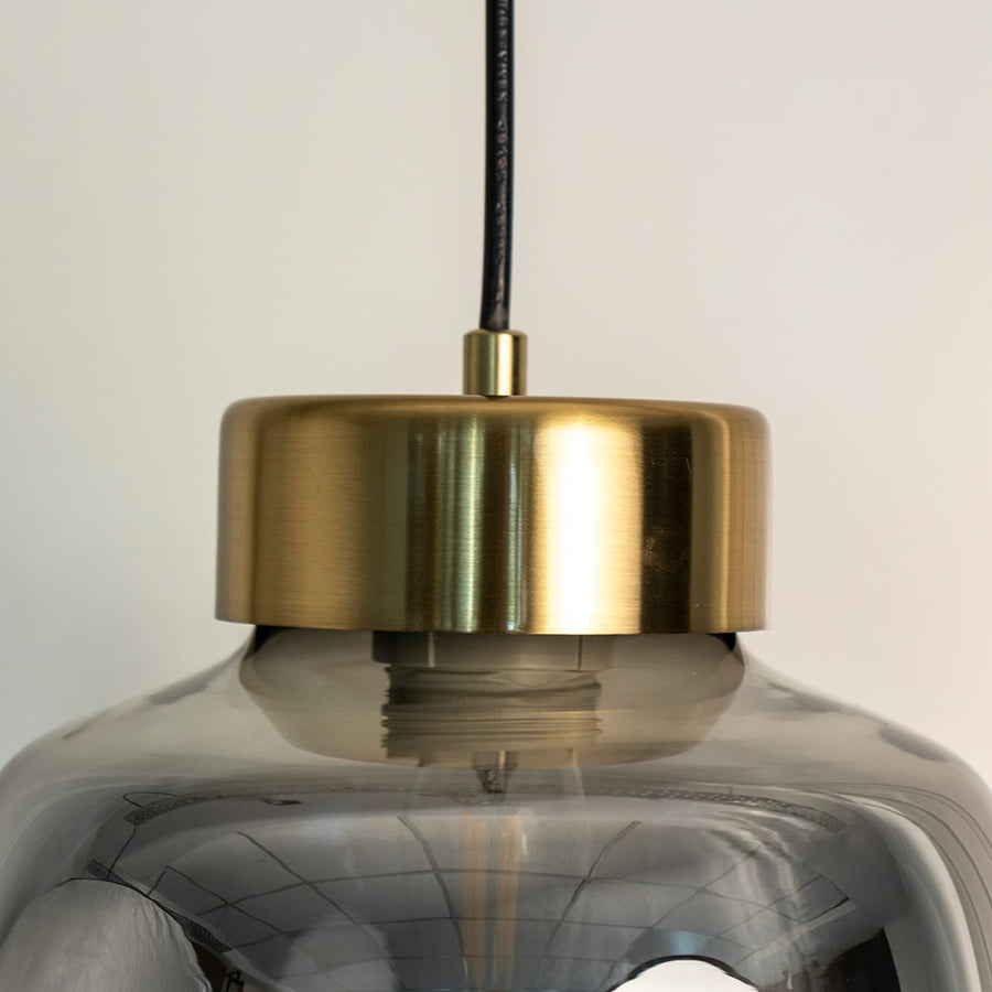 Smoked glass pendant lamp illuminated softly with golden glow turned off highlighting its tinted shade and modern metal detailing.