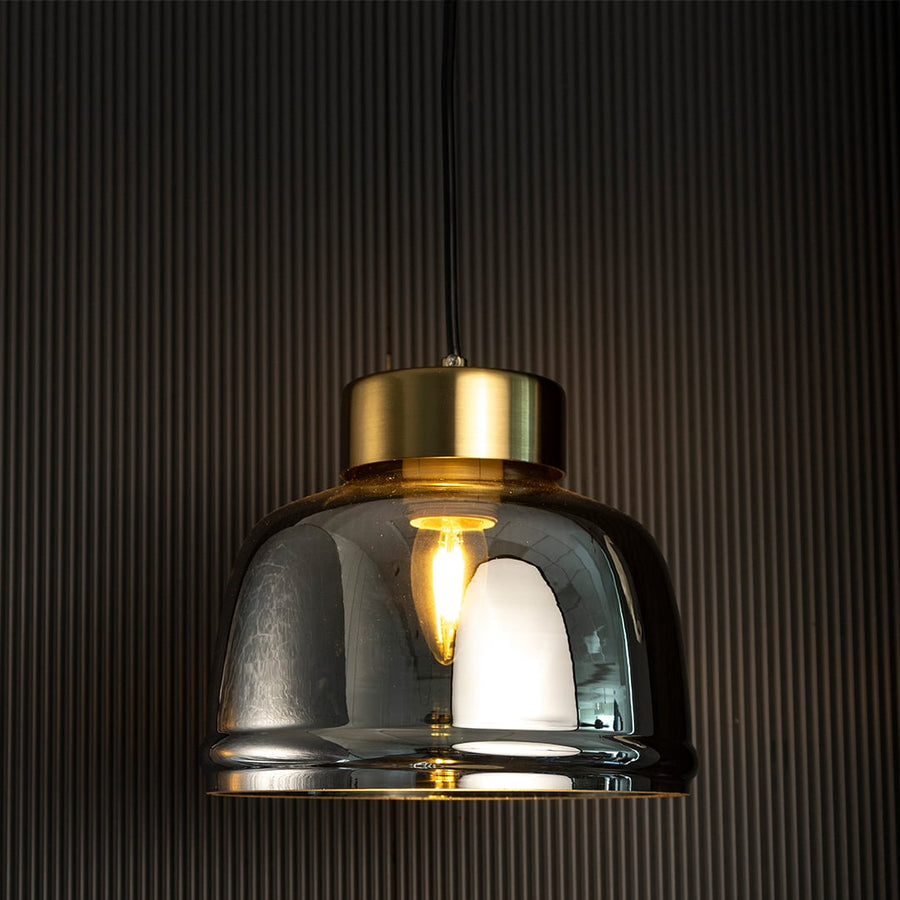 Smoked glass pendant light glowing through golden tinted shade creating a modern luxurious appeal on dark background.