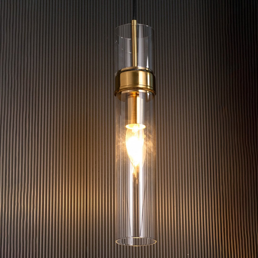 Tall cylindrical glass pendant light glowing warmly against a dark textured background adding depth and a premium modern feel to the lighting design.