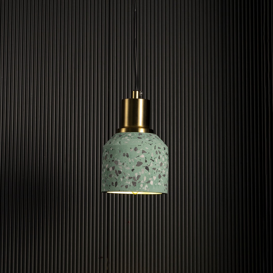 Grey terrazzo pendant light turned on with brass accent creating warm modern glow against black background.