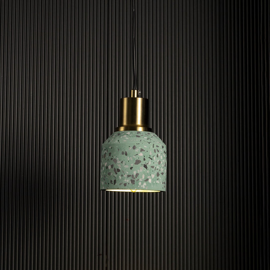 Grey terrazzo pendant light turned on with brass accent creating warm modern glow against black background.