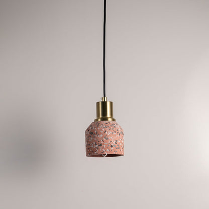 Pink terrazzo pendant light with brass top and black cord displayed against white wall.