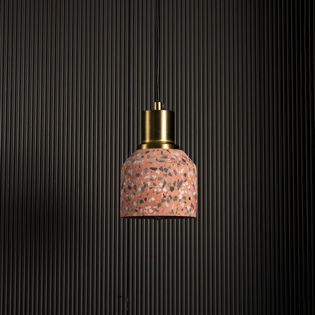Pink terrazzo pendant light with brass accent against black background for contemporary industrial interiors.