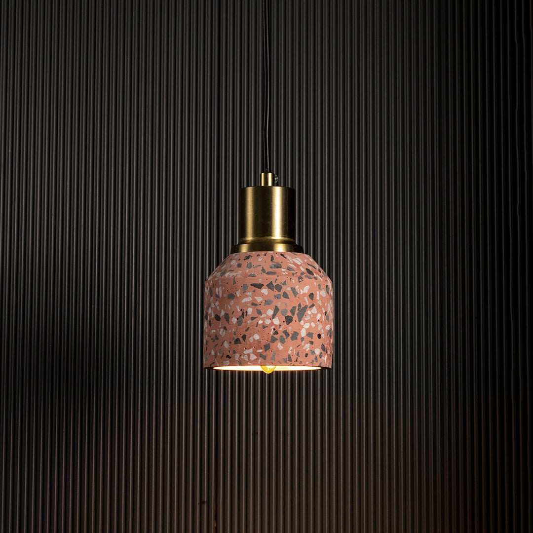 Pink terrazzo pendant light glowing warmly against dark background creating a cozy industrial lighting effect.