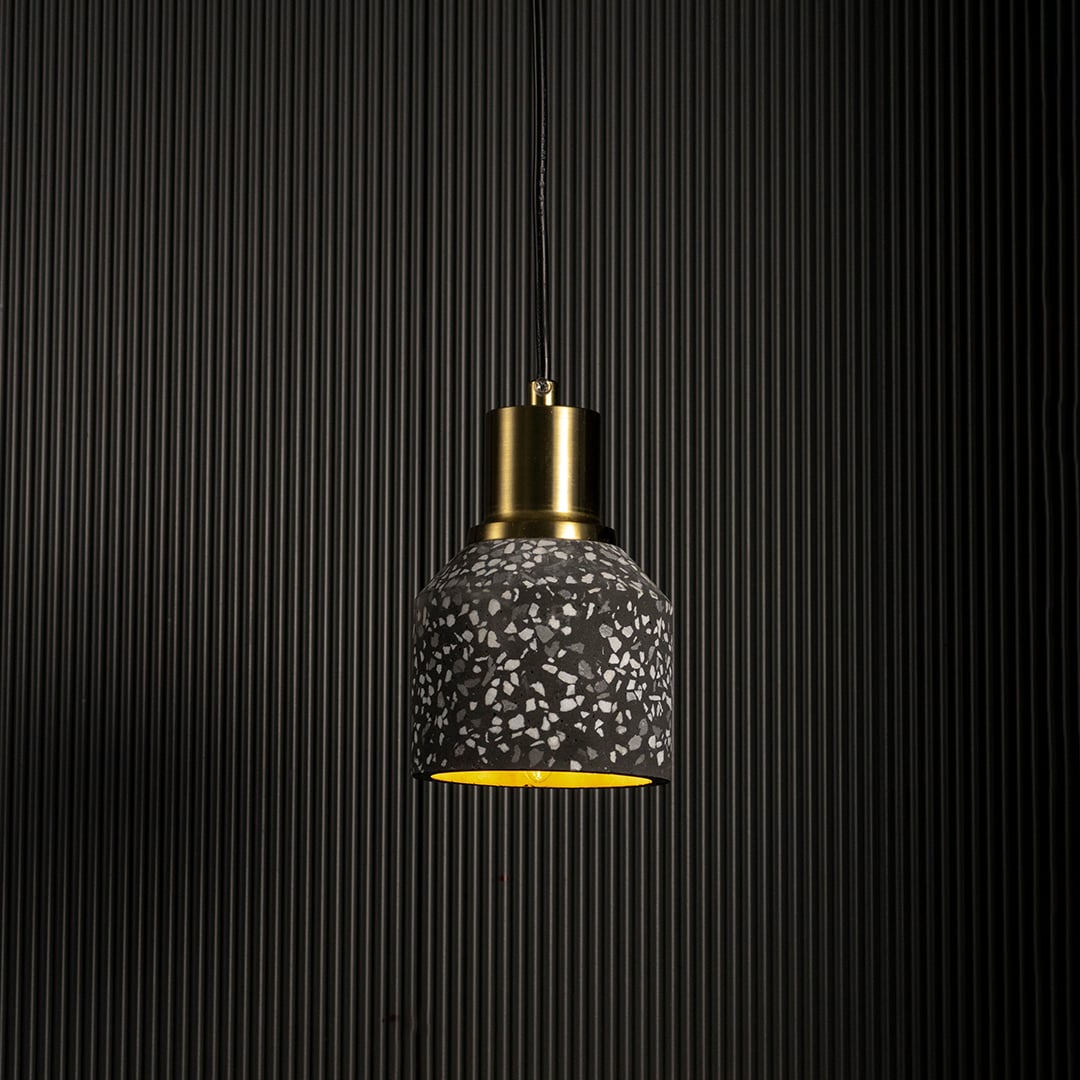 Handcrafted terrazzo pendant light softly illuminated to show its black speckled texture and modern brass top on a white background.