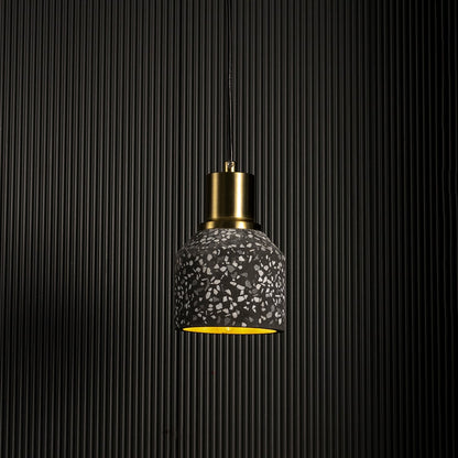 Handcrafted terrazzo pendant light softly illuminated to show its black speckled texture and modern brass top on a white background.