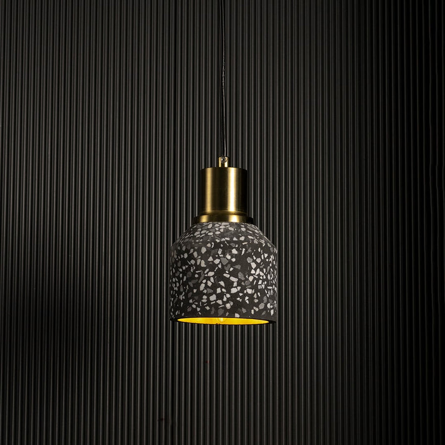 Handcrafted terrazzo pendant light softly illuminated to show its black speckled texture and modern brass top on a white background.