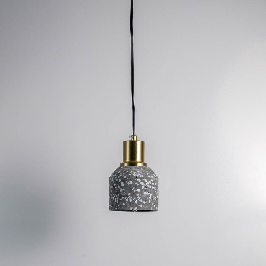 Minimal grey terrazzo pendant light with brass top and black cord against white wall for modern interiors.