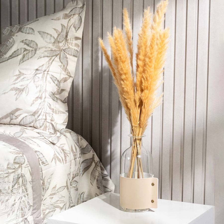 Elegant dried pampas grass in clear glass vase with beige leather strap styled on bedside table for home decor.