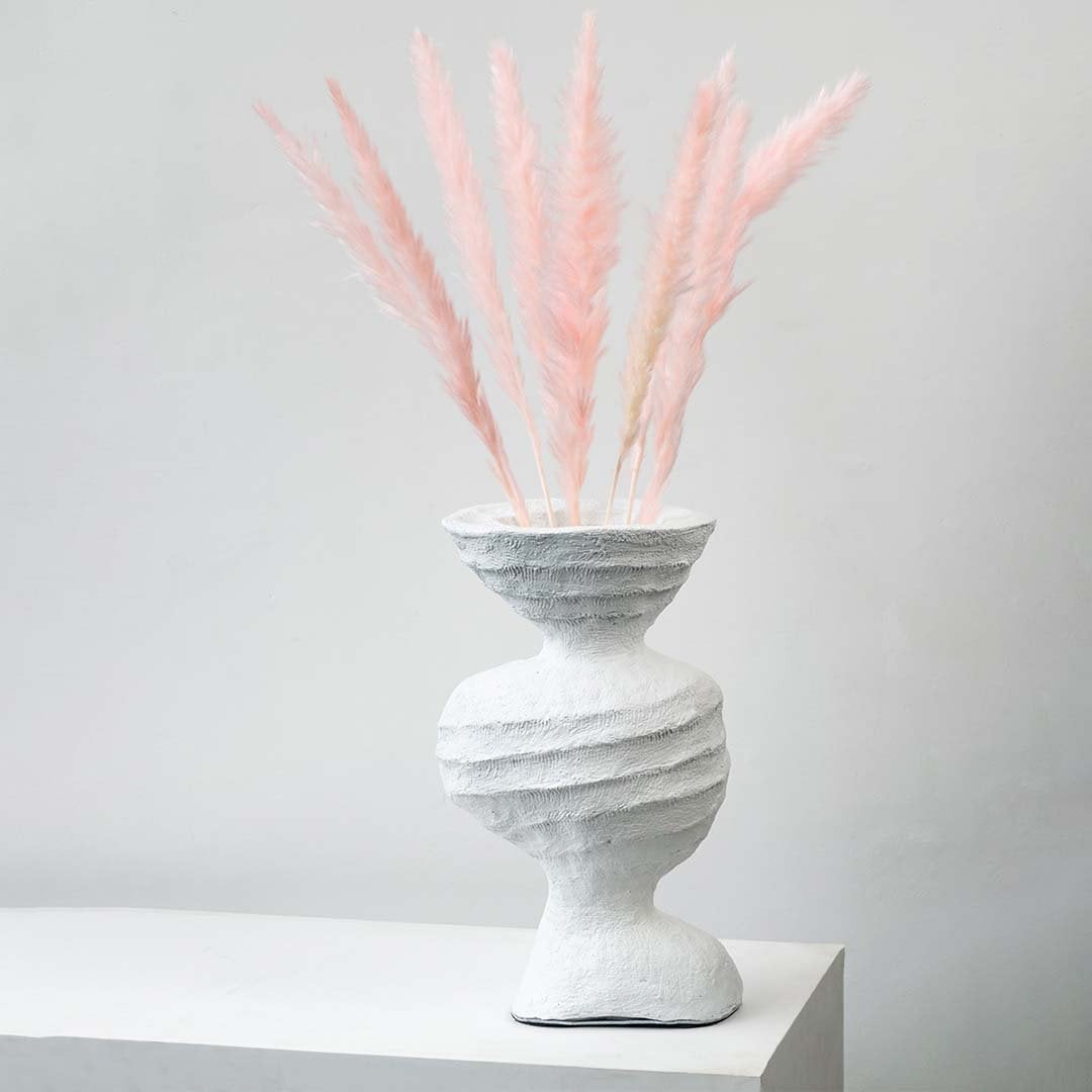 Light pink pampas grass stems styled in textured white ceramic vase elegant boho home decor on white backdrop
