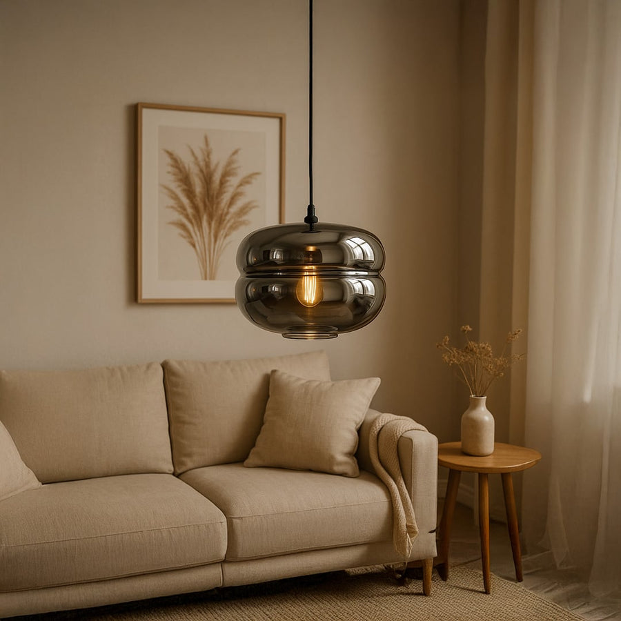Modern smoked glass pendant light with warm glowing bulb hanging above a beige sofa creating a cozy elegant ambience in a neutral living room setting.