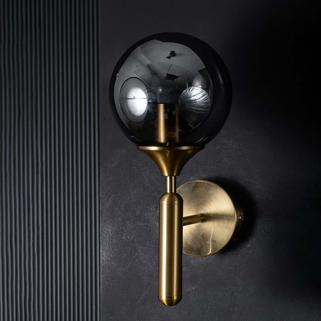 Gold and black glass wall light glowing warmly on a dark background showcasing its smoked glass shade and modern ambient lighting effect.