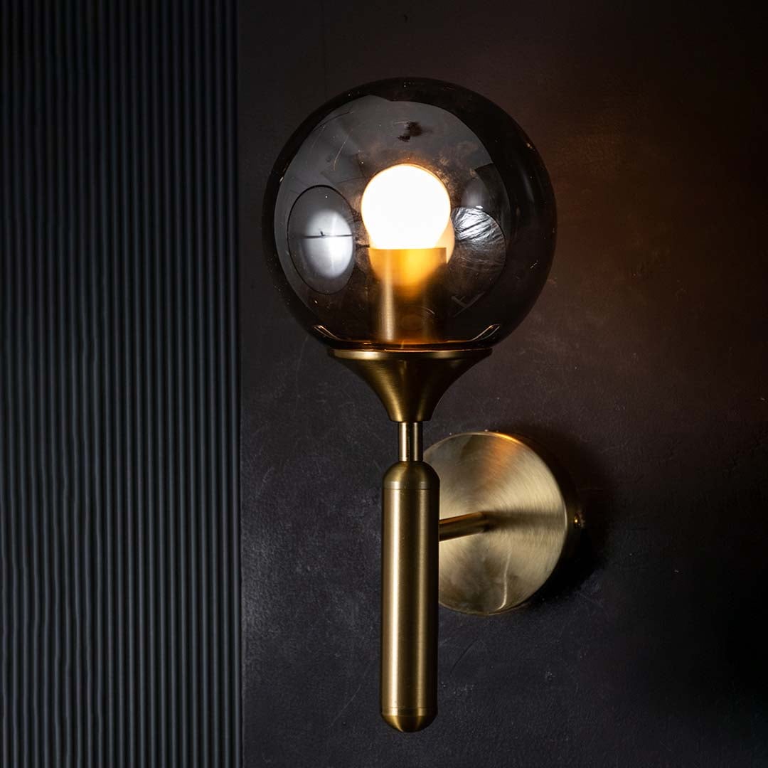 Gold and black glass wall light glowing warmly on a dark background showcasing its smoked glass shade and modern ambient lighting effect.