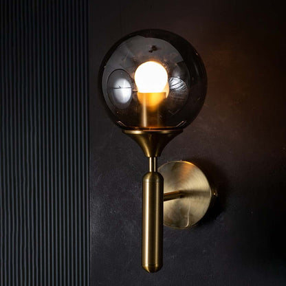 Gold and black glass wall light glowing warmly on a dark background showcasing its smoked glass shade and modern ambient lighting effect.
