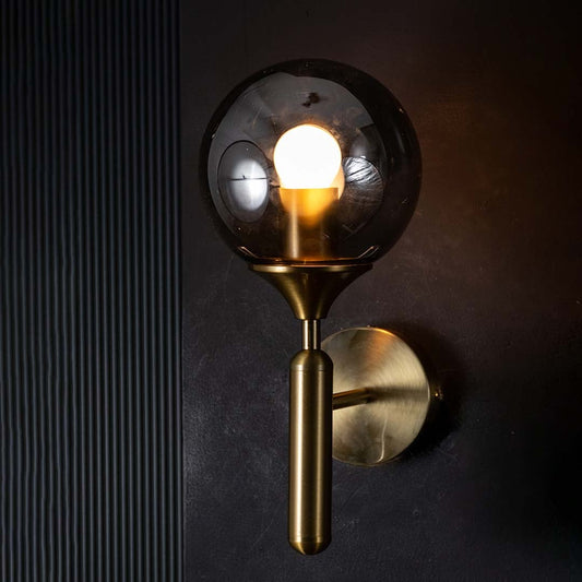 Gold and black glass wall light glowing warmly on a dark background showcasing its smoked glass shade and modern ambient lighting effect.