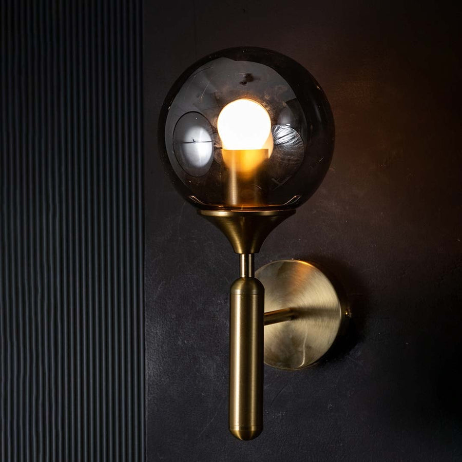 Gold and black glass wall light glowing warmly on a dark background showcasing its smoked glass shade and modern ambient lighting effect.