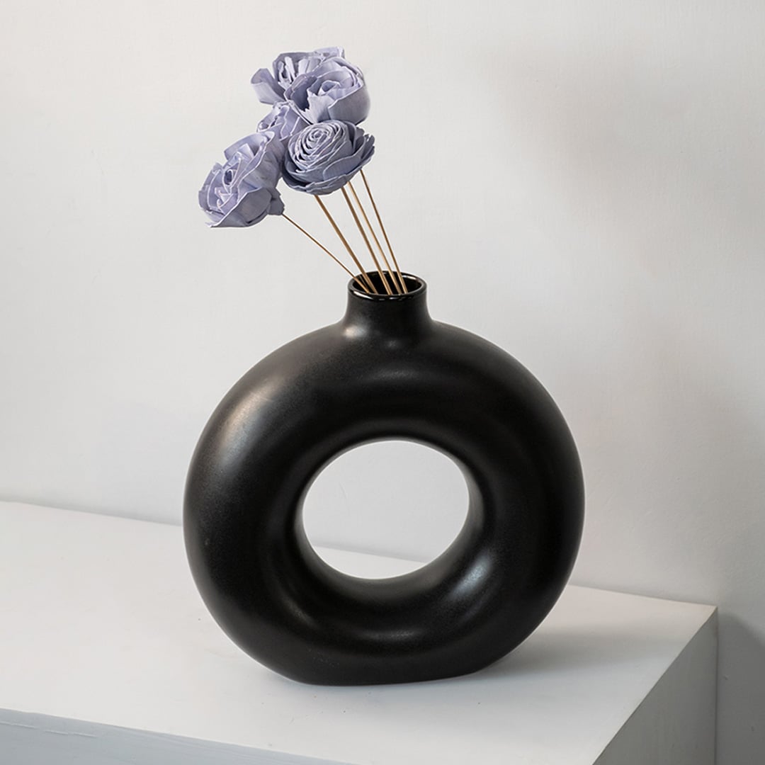 Black round ceramic vase with hole design styled with purple dried flower stems modern home table decor accent.