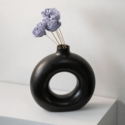 Black round ceramic vase with hole design styled with purple dried flower stems modern home table decor accent.