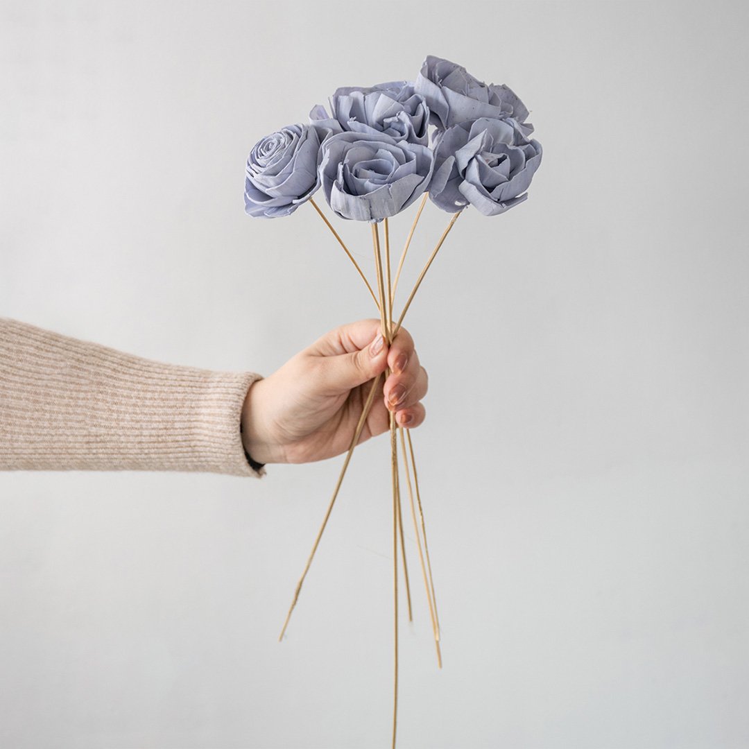 Hand holding a bundle of pastel lavender handmade sola wood flower stems for creative modern bedroom decor on white backdrop.