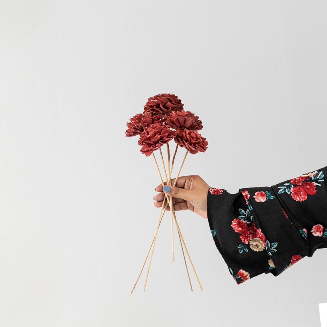 Hand holding a bundle of rust orange handmade sola wood flower stems for cozy autumnal tabletop vase decor on white backdrop.