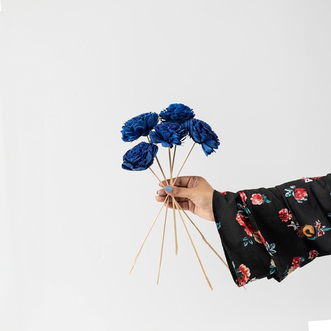 Hand holding a bundle of royal blue handmade sola wood flower stems for unique bohemian room vase decor on white backdrop.