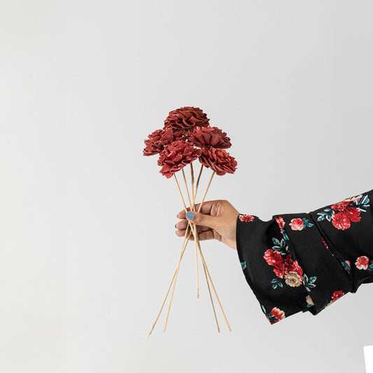 Hand holding a bundle of rust orange handmade sola wood flower stems for cozy autumnal tabletop vase decor on white backdrop.