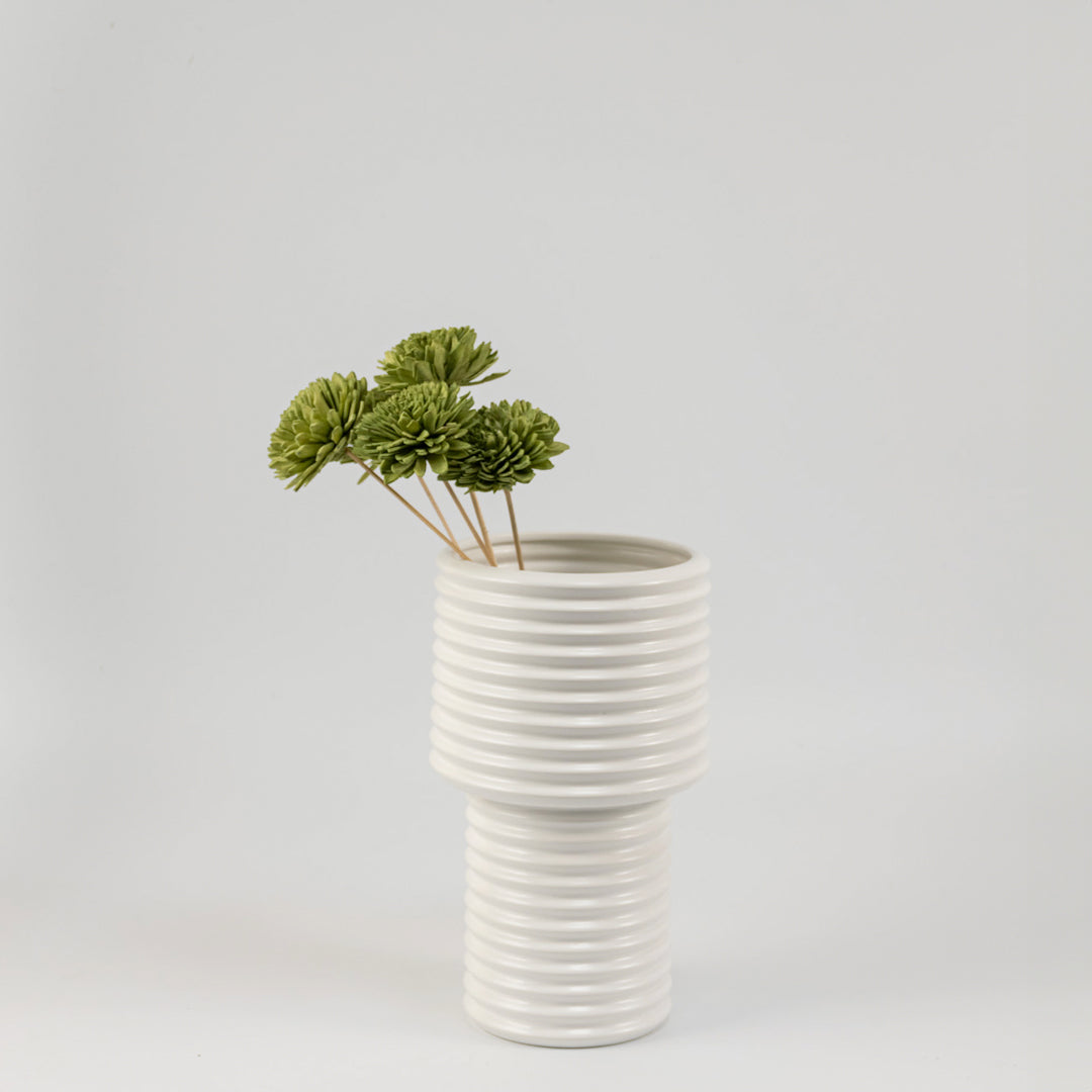 Moss green handmade sola wood flower stems arranged inside a modern white ribbed ceramic vase for bedroom tabletop decor.