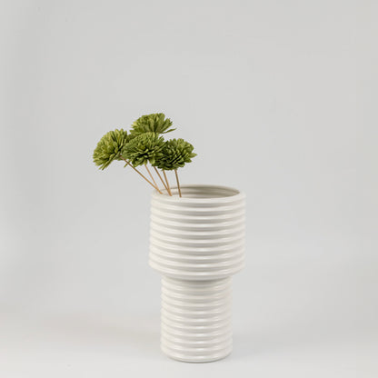 Moss green handmade sola wood flower stems arranged inside a modern white ribbed ceramic vase for bedroom tabletop decor.