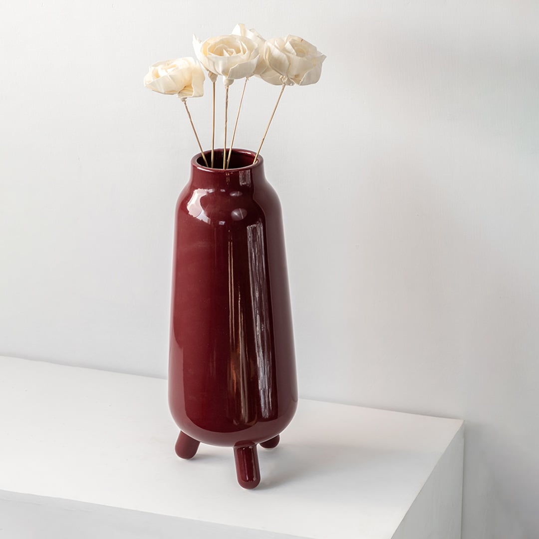 Elegant burgundy vase placed on a minimalist white shelf highlighting its tall structure and deep red hue for contemporary home décor.