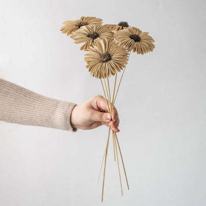 Hand holding five natural jute burlap handmade gerbera daisy flower stems for rustic farmhouse vase decor on white backdrop.