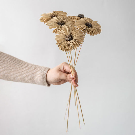 Hand holding five natural jute burlap handmade gerbera daisy flower stems for rustic farmhouse vase decor on white backdrop.