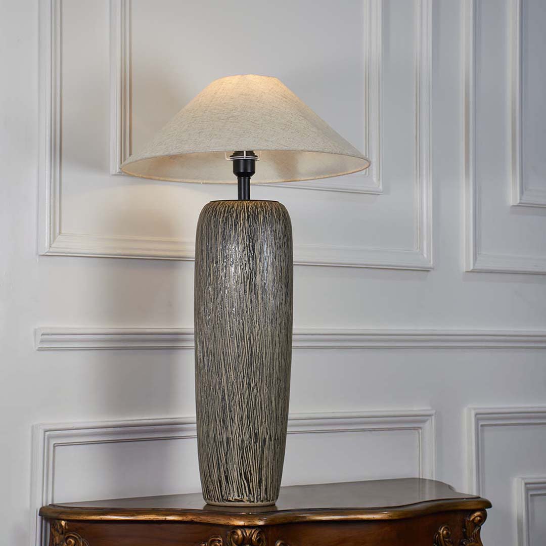 Textured ceramic table lamp with white fabric shade creating warm ambient lighting on elegant wooden console decor.