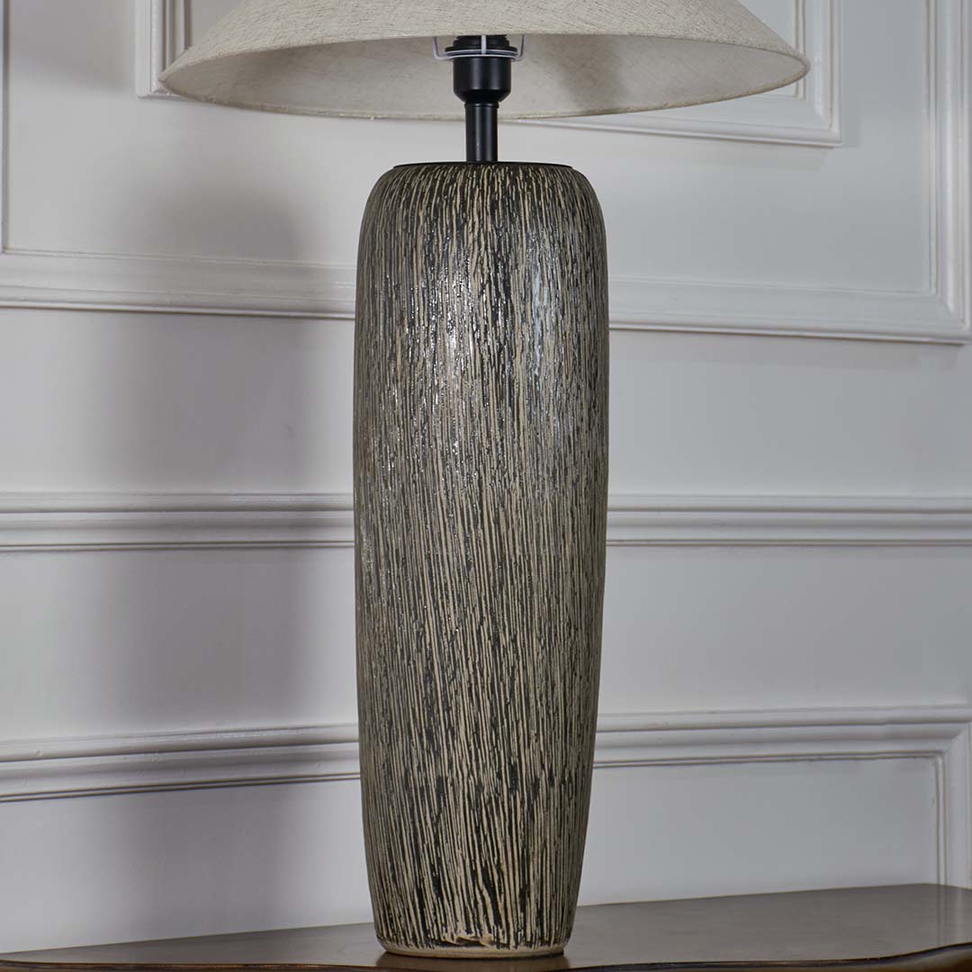 Closeup of tall grey ceramic floor lamp with detailed textured finish and wide beige shade showcasing artisan craftsmanship and refined style.