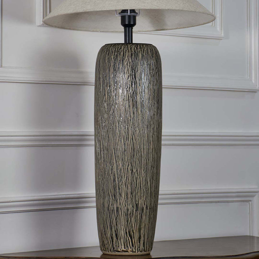 Closeup of tall grey ceramic floor lamp with detailed textured finish and wide beige shade showcasing artisan craftsmanship and refined style.