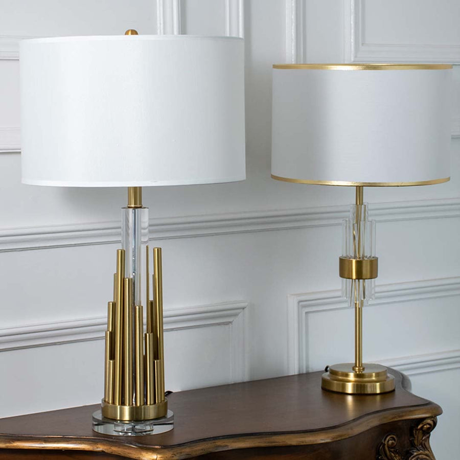 Gold metal table lamps with clean white drum shades shown together with lights off showcasing elegant sculpted bases for upscale interior styling.