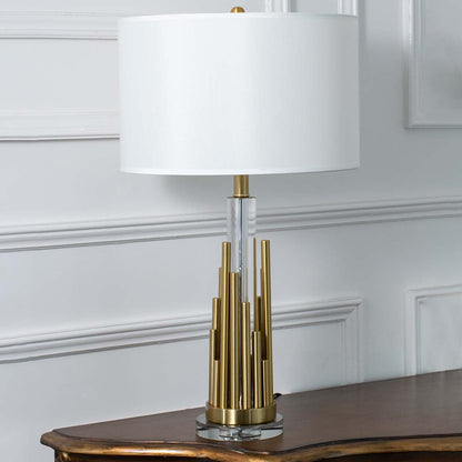 Gold metal table lamp with white drum shade and sculpted tiered base displayed on a white background perfect for modern home styling and console table decor.