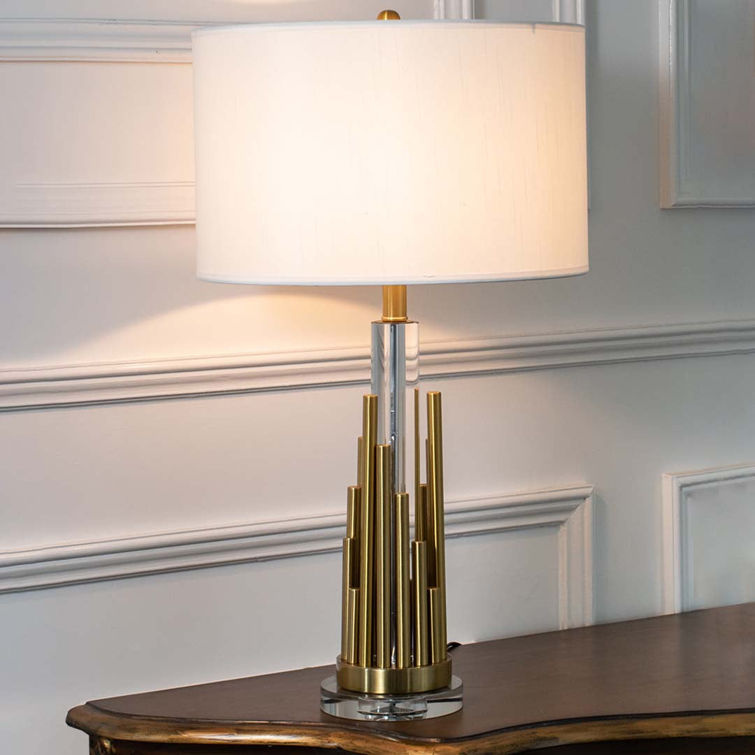 Gold metal table lamp with fabric drum shade and geometric base creating refined modern ambient lighting for interiors.