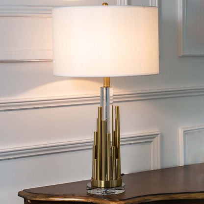 Gold metal table lamp with fabric drum shade and geometric base creating refined modern ambient lighting for interiors.