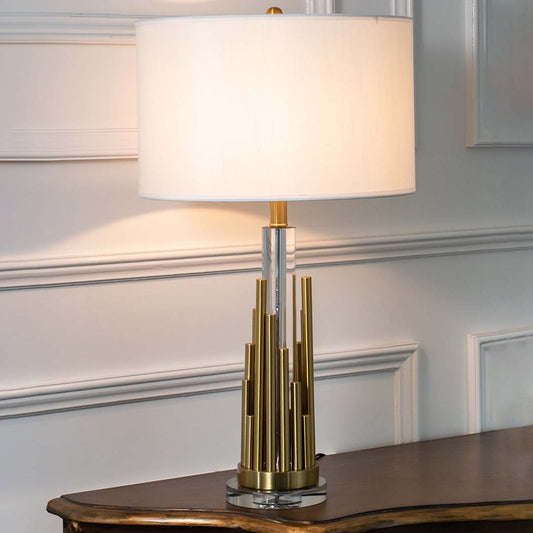 Gold metal table lamp with fabric drum shade and geometric base creating refined modern ambient lighting for interiors.