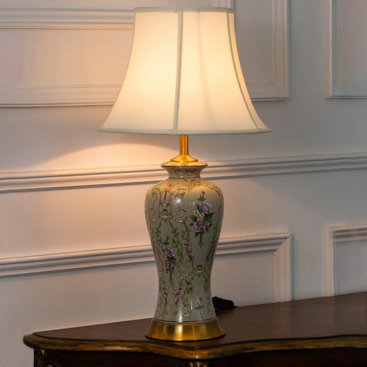 Ivory ceramic lamp with floral design and golden base displayed with light on against white background decor styling.
